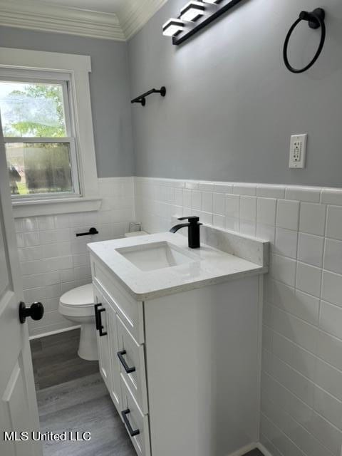 bathroom featuring toilet, tile walls, vanity, hardwood / wood-style flooring, and ornamental molding