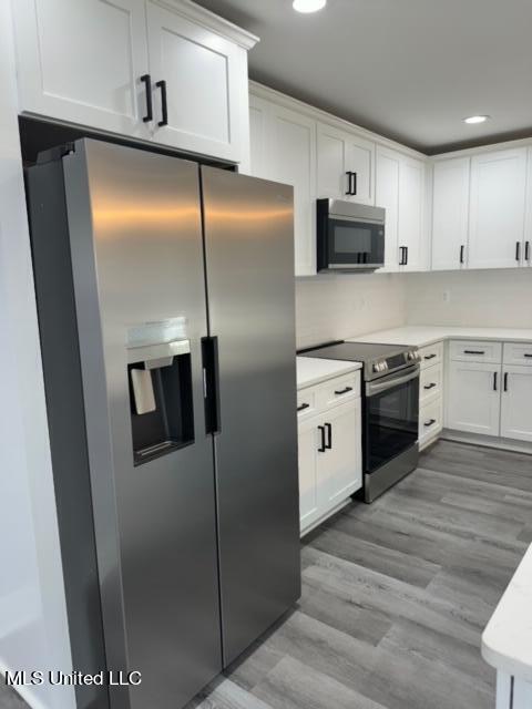 kitchen with appliances with stainless steel finishes, white cabinets, and light wood-type flooring