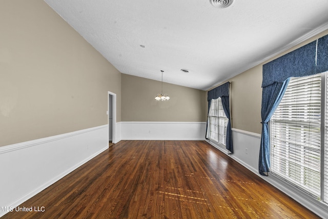 spare room with vaulted ceiling, plenty of natural light, dark wood-type flooring, and a notable chandelier