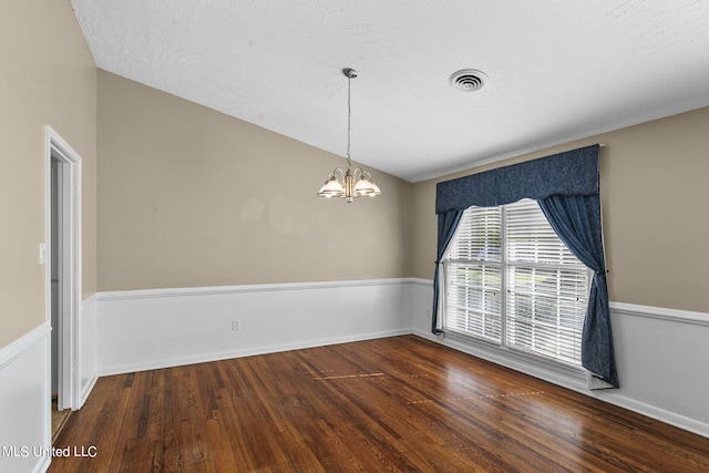 empty room featuring a textured ceiling, dark wood-type flooring, vaulted ceiling, and an inviting chandelier