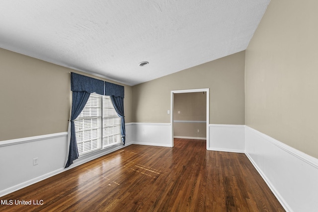 empty room featuring a textured ceiling, dark wood-type flooring, and lofted ceiling