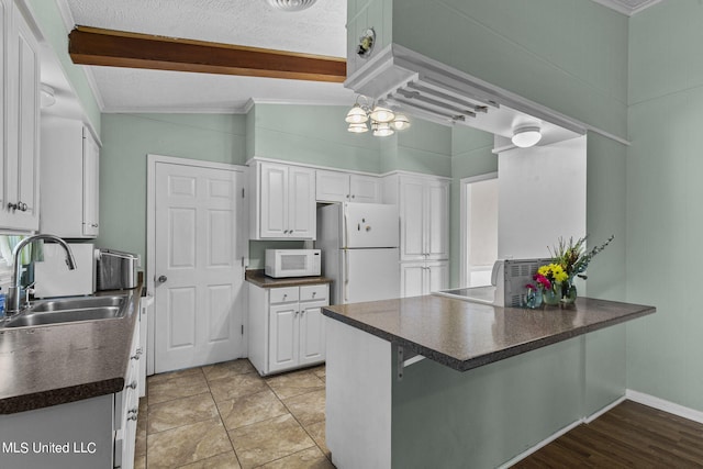 kitchen with kitchen peninsula, white appliances, vaulted ceiling, sink, and white cabinets