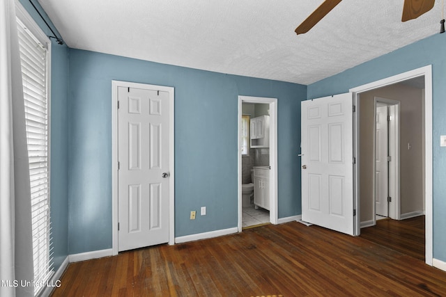 unfurnished bedroom with ceiling fan, a textured ceiling, connected bathroom, dark hardwood / wood-style flooring, and a closet