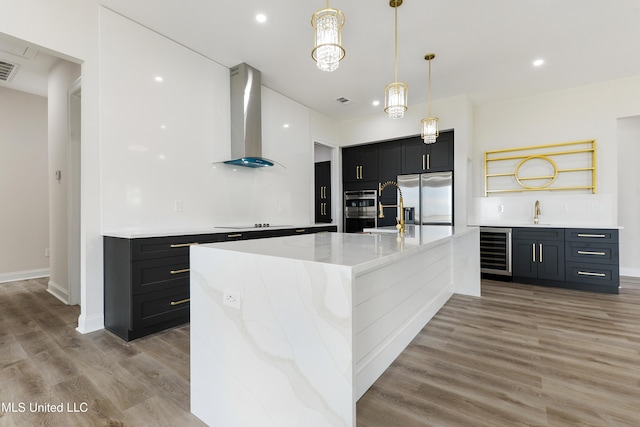 kitchen featuring light wood-type flooring, stainless steel appliances, beverage cooler, wall chimney range hood, and a large island