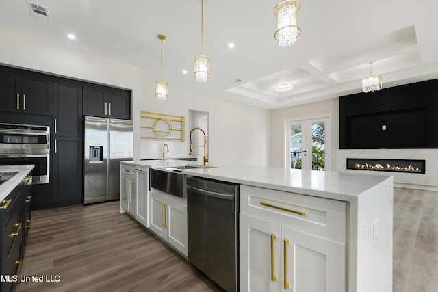 kitchen with appliances with stainless steel finishes, decorative light fixtures, a kitchen island with sink, white cabinets, and hardwood / wood-style flooring