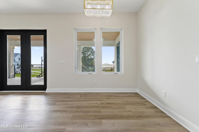 spare room with hardwood / wood-style flooring, a notable chandelier, and french doors