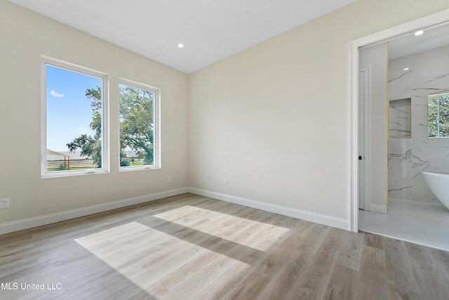 unfurnished bedroom with ensuite bath, light wood-type flooring, and multiple windows