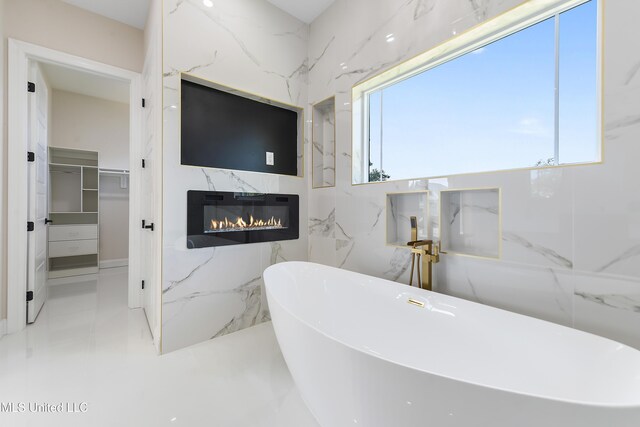 bathroom featuring a high end fireplace, plenty of natural light, a bathing tub, and tile walls