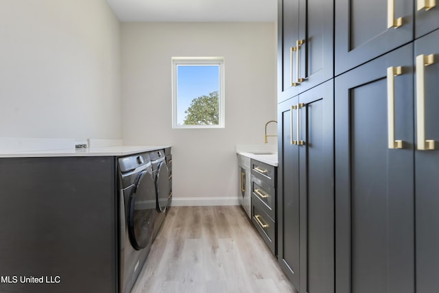 clothes washing area with washer and clothes dryer, light hardwood / wood-style floors, cabinets, and sink