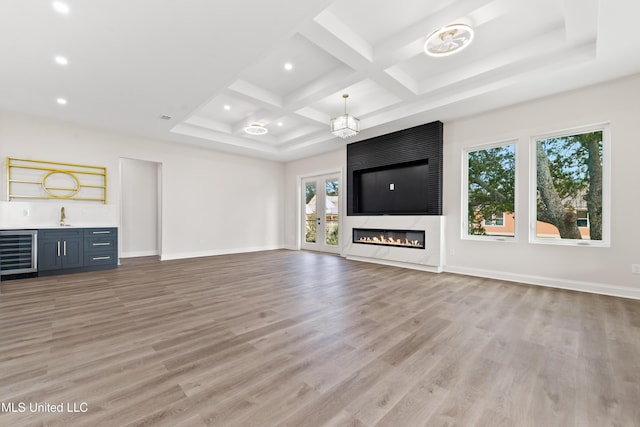 unfurnished living room featuring coffered ceiling, a large fireplace, beamed ceiling, light hardwood / wood-style floors, and wine cooler