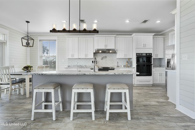 kitchen with under cabinet range hood, visible vents, tasteful backsplash, and dobule oven black