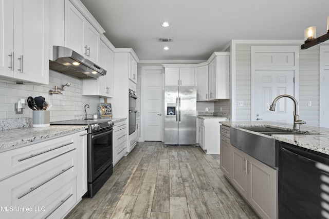 kitchen with a sink, black appliances, white cabinets, under cabinet range hood, and light wood-type flooring