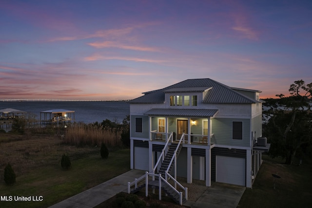 coastal inspired home featuring a water view, driveway, stairway, covered porch, and a garage