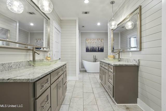 bathroom featuring a freestanding bath, two vanities, visible vents, and a sink