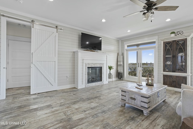 living area featuring a glass covered fireplace, wood finished floors, recessed lighting, a barn door, and crown molding