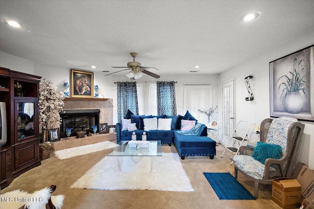 living room featuring a tile fireplace, light carpet, ceiling fan, and a textured ceiling