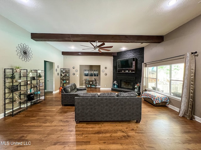 living room featuring ceiling fan, hardwood / wood-style flooring, beam ceiling, and a brick fireplace