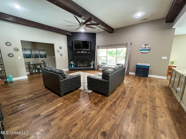 living room with ceiling fan, beamed ceiling, dark hardwood / wood-style flooring, and a fireplace