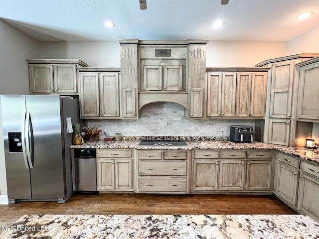 kitchen featuring dark hardwood / wood-style flooring, stainless steel fridge, black gas cooktop, light stone counters, and decorative backsplash