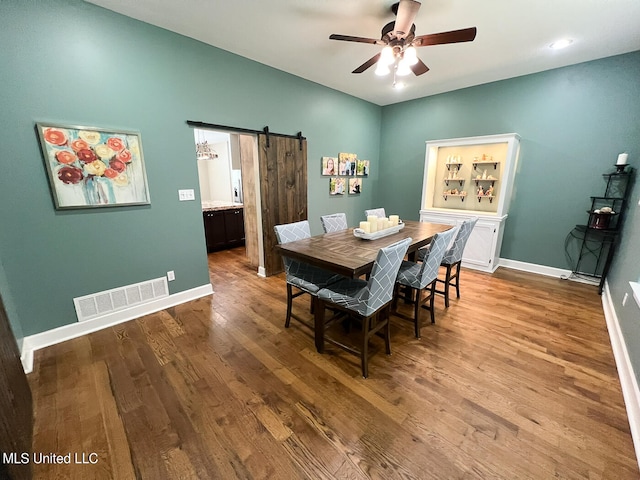 dining room featuring a barn door, hardwood / wood-style flooring, and ceiling fan