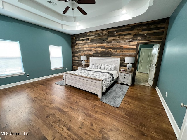 unfurnished bedroom featuring wooden walls, ceiling fan, dark wood-type flooring, and a raised ceiling