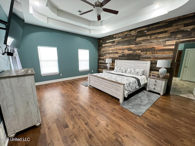 unfurnished bedroom featuring wood walls, ceiling fan, dark wood-type flooring, and a raised ceiling