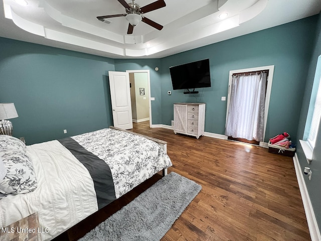 bedroom with ceiling fan, a tray ceiling, and dark hardwood / wood-style flooring