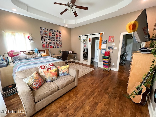 bedroom featuring dark hardwood / wood-style floors, a barn door, ceiling fan, and a raised ceiling