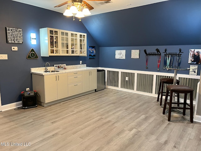 bar with sink, ceiling fan, vaulted ceiling, and light wood-type flooring