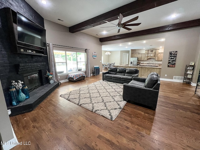 living room with hardwood / wood-style floors, beam ceiling, ceiling fan with notable chandelier, and a fireplace