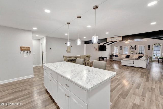 kitchen featuring pendant lighting, white cabinetry, a center island, light stone countertops, and light wood-type flooring