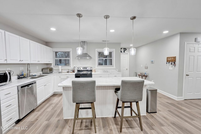 kitchen with a kitchen island, appliances with stainless steel finishes, decorative light fixtures, white cabinets, and wall chimney exhaust hood