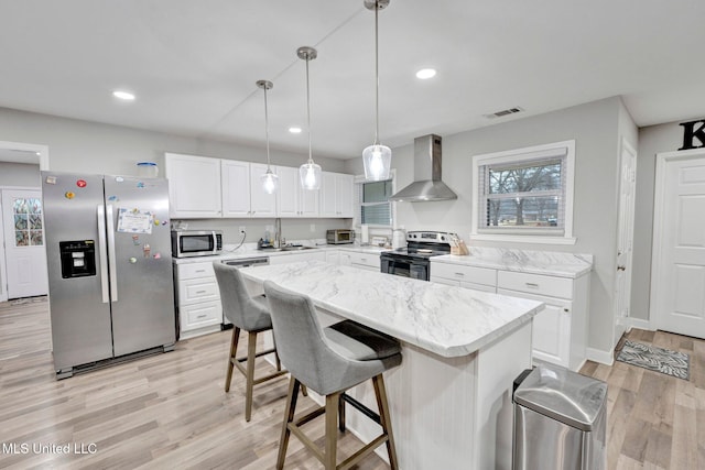 kitchen with a kitchen island, appliances with stainless steel finishes, white cabinets, hanging light fixtures, and wall chimney exhaust hood