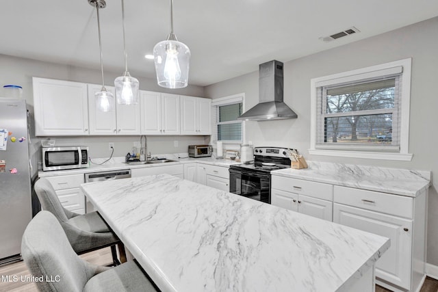 kitchen with sink, appliances with stainless steel finishes, white cabinetry, hanging light fixtures, and wall chimney exhaust hood