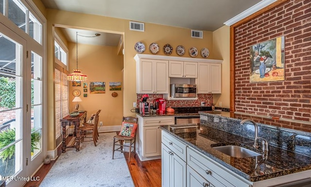 kitchen with a kitchen island with sink, sink, light hardwood / wood-style flooring, dark stone countertops, and white cabinets