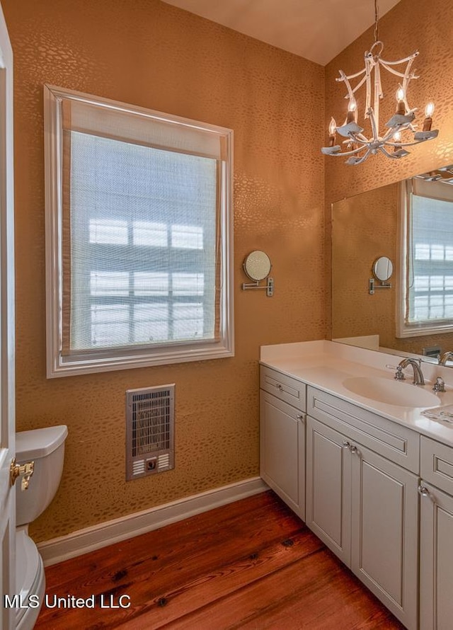 bathroom with vanity, heating unit, hardwood / wood-style flooring, an inviting chandelier, and toilet