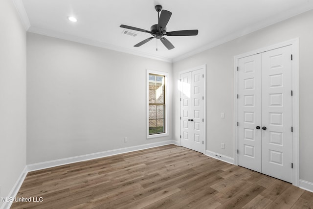 unfurnished bedroom featuring ceiling fan, ornamental molding, two closets, and hardwood / wood-style flooring