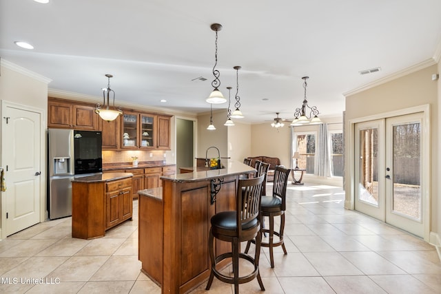 kitchen featuring stainless steel fridge, a center island with sink, visible vents, and brown cabinets