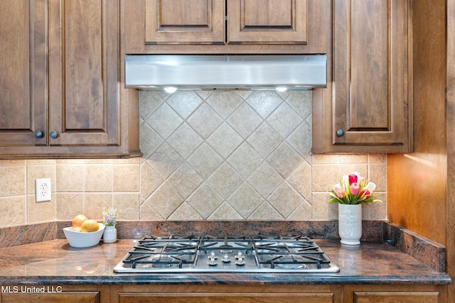 kitchen featuring dark countertops, wall chimney exhaust hood, stainless steel gas stovetop, and tasteful backsplash