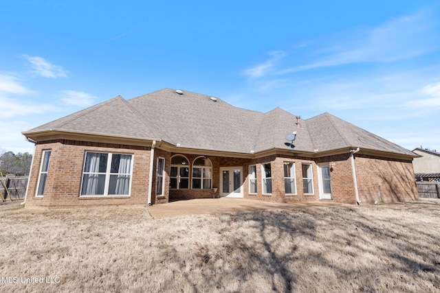 rear view of property featuring brick siding, roof with shingles, and fence