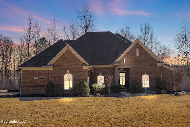 view of front of home with brick siding, a front lawn, and fence