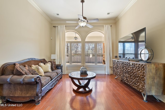 living room with crown molding, visible vents, a ceiling fan, baseboards, and hardwood / wood-style flooring