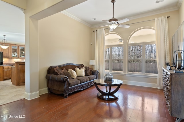 living area featuring a ceiling fan, crown molding, baseboards, and wood finished floors