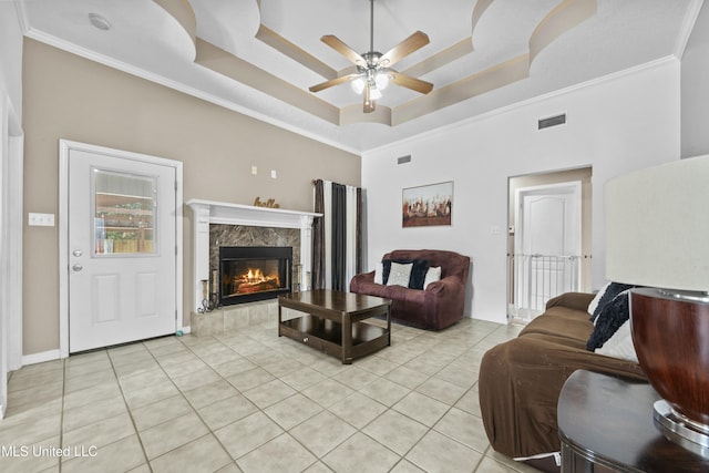 tiled living room featuring a high end fireplace, a raised ceiling, ornamental molding, and ceiling fan