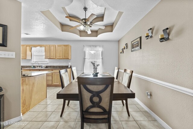 tiled dining room with a textured ceiling, ceiling fan, a tray ceiling, and sink