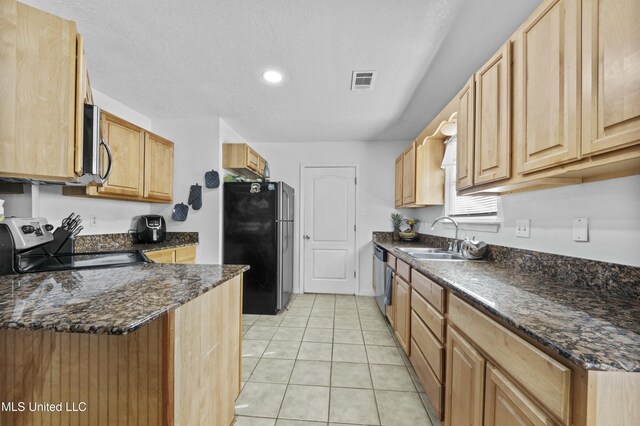 kitchen featuring dark stone countertops, stainless steel appliances, light brown cabinetry, sink, and light tile patterned flooring