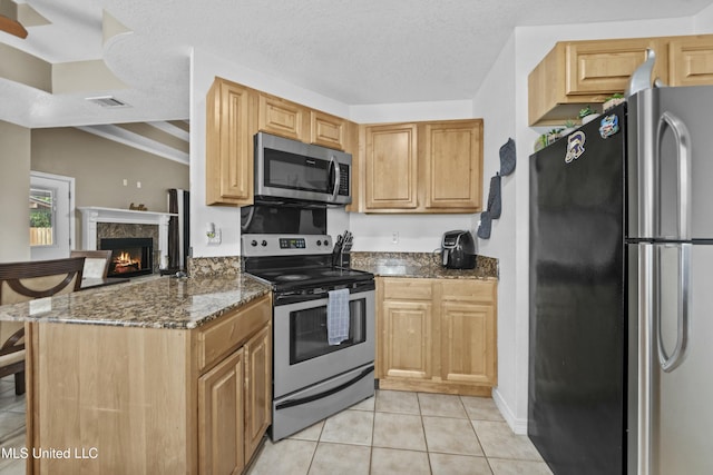 kitchen featuring appliances with stainless steel finishes, a premium fireplace, light tile patterned floors, dark stone counters, and a textured ceiling