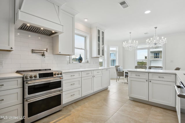 kitchen with premium range hood, hanging light fixtures, ornamental molding, range with two ovens, and white cabinets