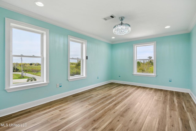 empty room featuring ornamental molding, plenty of natural light, a chandelier, and light wood-type flooring