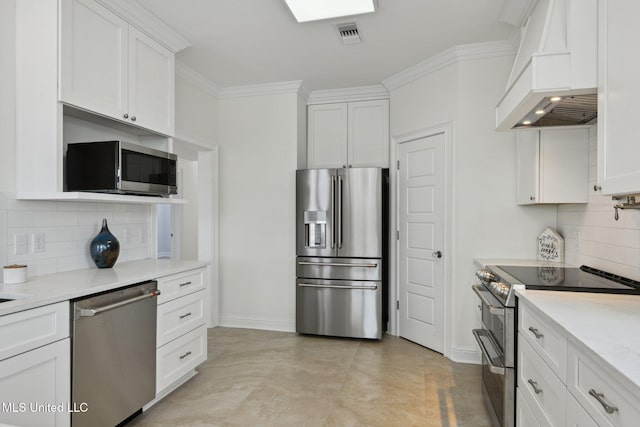 kitchen featuring premium range hood, crown molding, stainless steel appliances, light stone countertops, and white cabinets